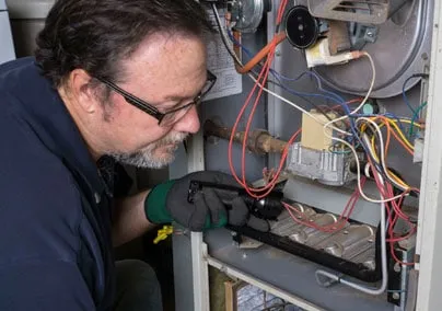 A technician inspecting the internal components of a heating system, focusing on wires and other parts.